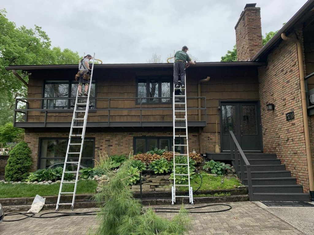 K-Guard installers on ladders fitting gutter and hood along the fascia of a brick and cedar Central Ohio home