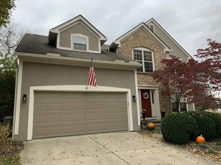 White hooded gutter protection on a stucco and brick Central Ohio home with fall leaves on the driveway